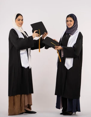Success, hard work and excellence, looking at the camera with gestures of happiness and pride, celebrating university graduation with friends, portrait of two Arab Gulf Emirati university graduates wearing graduation attire and holding graduation caps, full body length, white background