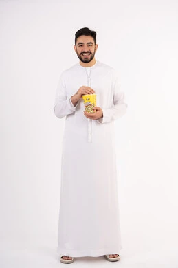 مفهوم التسليه والترفيه، تعابير المرح والاستمتاع ، الاستمتاع بتناول الفوشار، قضاء أوقات ممتعة ومسلية، بورتريه لرجل عربي خليجي اماراتي يرتدي الزى التقليدي يحمل بيده علبة الفشار ويقوم بمشاهده الافلام ، مشاهدة فيلم سينمائي ، خلفيه بيضاء