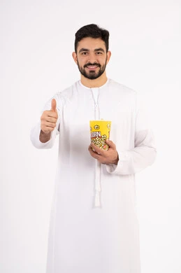 Raising index finger in approval gesture, expressions of quality, excellence and satisfaction, having a fun and entertaining time, the concept of entertainment and recreation, portrait of an Arab Gulf Emirati man wearing traditional clothing holding a box of popcorn and watching movies, watching a movie, white background