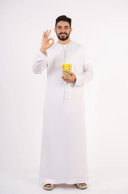 قضاء أوقات ممتعة ومسلية، تعابير الجودة والامتياز والرضي ،  رفع اليد بايماءات الموافقه ، مفهوم التسليه والترفيه، بورتريه لرجل عربي خليجي اماراتي يرتدي الزى التقليدي يحمل بيده علبة الفشار ويقوم بمشاهده الافلام ، مشاهدة فيلم سينمائي ، خلفيه بيضاء