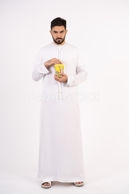 إيماءات وجه ويدين تدل على الغضب ، قضاء أوقات ممتعة ، مفهوم التسليه والترفيه، رجل عربي خليجي اماراتي يرتدي الزى التقليدي يحمل بيده علبة الفشار ويقوم بمشاهده الافلام ، مشاهدة فيلم سينمائي