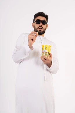 تعابير الخوف والرعب ، مشاهدة الأفلام والعروض المسرحية في السينما، قضاء وقت ممتع بتناول الفشار اثناء مشاهده التلفاز ، بورتريه لصديقان عربيان خليجيان امارتيان يرتديان الكندوره والغتره يشاهدان الافلام ، يحملان بيدهما أكواب مليئه بالبوب كورن، مفهوم التسليه والترفيه الجماعيه ، خلفيه بيضاء