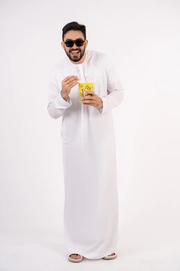 قضاء أوقات ممتعة ومسلية،  إيماءات وجه ويدين تدل على السعادة والمتعة، بورتريه لرجل عربي خليجي اماراتي يرتدي الكندوره والغتره يحمل بيده علبة الفشار ومستمتع بمشاهدة الأفلام ، مشاهدة فيلم سينمائي، مفهوم التسليه والترفيه ، خلفيه بيضاء