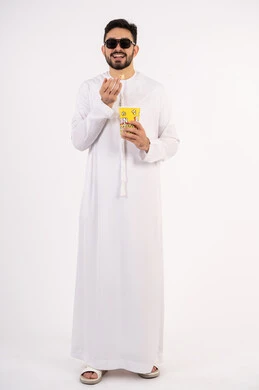 مشاهدة فيلم سينمائي ، الاستمتاع بتناول البوب كورن ،مفهوم التسليه والترفيه،  قضاء أوقات ممتعة ومسلية، بورتريه لرجل عربي خليجي اماراتي يرتدي الزى التقليدي يحمل بيده علبة الفشار ويقوم بمشاهده الافلام ، خلفيه بيضاء