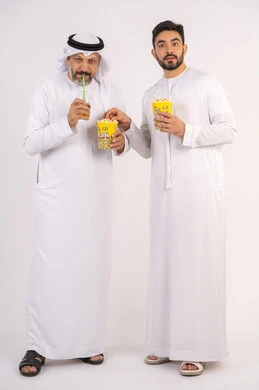 بورتريه لصديقان عربيان خليجيان امارتيان يرتديان الكندوره والغتره يشاهدان الافلام ، يحملان بيدهما أكواب مليئه بالبوب كورن، مشاهدة الأفلام والعروض المسرحية في السينما،  قضاء وقت ممتع بتناول الفشار اثناء مشاهده التلفاز ،  تعابير الصدمه والذهول، مفهوم التسليه والترفيه الجماعيه ، خلفيه بيضاء
