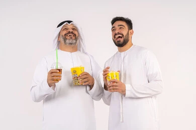 بورتريه لصديقان عربيان خليجيان امارتيان يرتديان الكندوره والغتره يشاهدان الافلام ، يحملان بيدهما أكواب مليئه بالبوب كورن، مشاهدة الأفلام والعروض المسرحية في السينما،المرح مع الاصدقاء ، شرب المشروبات البارده، قضاء اوقات ممتعه مع الاصدقاء، مفهوم التسليه والترفيه الجماعيه ،  تناول الفشار اثناء مشاهده التلفاز ، خلفيه بيضاء