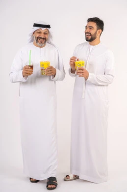 شرب المشروبات البارده، قضاء اوقات ممتعه مع الاصدقاء، مفهوم التسليه والترفيه الجماعيه ، تعابير المرح والسرور ، مشاهدة الأفلام والعروض المسرحية في السينما، بورتريه لصديقان عربيان خليجيان امارتيان يرتديان الكندوره والغتره يشاهدان الافلام ، يحملان بيدهما أكواب مليئه بالبوب كورن،  تناول الفشار اثناء مشاهده التلفاز ، خلفيه بيضاء