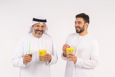 قضاء اوقات ممتعه مع الاصدقاء، مفهوم التسليه والترفيه الجماعيه ، تعابير المرح والسرور ، مشاهدة الأفلام والعروض المسرحية في السينما، بورتريه لصديقان عربيان خليجيان امارتيان يرتديان الكندوره والغتره يشاهدان الافلام ، يحملان بيدهما أكواب مليئه بالبوب كورن، شرب المشروبات البارده، تناول الفشار اثناء مشاهده التلفاز ، خلفيه بيضاء