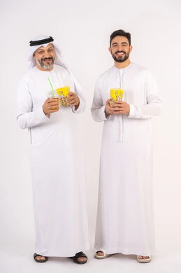 تعابير المرح والسرور ، مفهوم التسليه والترفيه الجماعيه ، مشاهدة الأفلام والعروض المسرحية في السينما، بورتريه لصديقان عربيان خليجيان امارتيان يرتديان الكندوره والغتره يشاهدان الافلام ، يحملان بيدهما أكواب مليئه بالبوب كورن، شرب المشروبات البارده، قضاء وقت ممتع بتناول الفشار اثناء مشاهده التلفاز ، خلفيه بيضاء