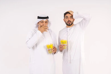 عدم معرفه ونسيان شئ ما ،  تعابير الصدمه والمفاجأه ، مشاهدة الأفلام في السينما، قضاء وقت ممتع ، بورتريه  لصديقان عربيان خليجيان امارتيان يرتديان الكندوره والغتره يشاهدان الافلام ، يحملان بيدهما أكواب مليئه بالبوب كورن، مفهوم التسليه والترفيه الجماعيه ، خلفيه بيضاء