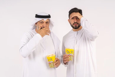محاوله رؤيه شئ بعيد ، مشاهدة الأفلام والعروض المسرحية في السينما، قضاء وقت ممتع بتناول الفشار اثناء مشاهده التلفاز ، بورتريه  لصديقان عربيان خليجيان امارتيان يرتديان الكندوره والغتره يشاهدان الافلام ، يحملان بيدهما أكواب مليئه بالبوب كورن، مفهوم التسليه والترفيه الجماعيه ، خلفيه بيضاء