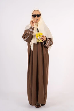 الاستمتاع باكل البوب كورن ، متابعه الفيلم المفضل ، مشاهدة الأفلام داخل السينما، التسلية والترفيه بقضاء أوقات ممتعة، بورتريه لامرأة عربية خليجية اماراتيه محجبة ترتدي عباءه وتحمل علبه فوشار ، خلفية بيضاء