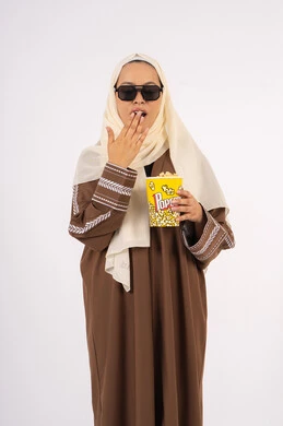 تعابير التعب والارهاق ، الحاجه الى النعاس والراحه ، بورتريه لامرأة عربية خليجية اماراتيه محجبة ترتدي عباءه وتحمل علبه فوشار ، متابعة الفيلم المفضل ، الاستمتاع باكل البوب كورن، مشاهدة الأفلام داخل السينما، التسلية والترفيه بقضاء أوقات ممتعة، خلفية بيضاء