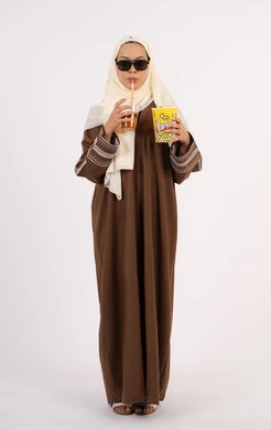 تعابير الاندماج والتفاعل ، شرب المشروبات المنعشه ، اكل البوب كورن ، قضاء أوقات ممتعة ، الاستمتاع بمشاهدة الأفلام داخل السينما، مفهوم التسلية والترفيه ، بورتريه لامرأة عربية خليجية اماراتيه محجبة ترتدي عباءه وتحمل علبه فوشار ، خلفية بيضاء