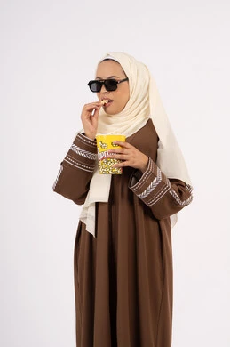 متابعة الفيلم المفضل ، الاستمتاع باكل البوب كورن ،مشاهدة الأفلام داخل السينما،التسلية والترفيه بقضاء أوقات ممتعة، بورتريه لامرأة عربية خليجية اماراتيه محجبة ترتدي عباءه وتحمل علبه فوشار ، خلفية بيضاء
