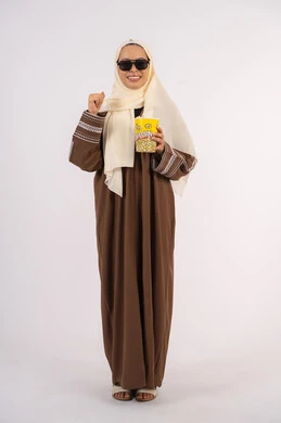 رفع قبضة اليد بتعابير الفوز والانتصار ، بورتريه لامرأة عربية خليجية اماراتيه محجبة ترتدي عباءه ، تحمل كيس الفوشار، متابعة الفيلم المفضل، التسلية والترفيه بقضاء أوقات ممتعة، الاستمتاع بمشاهدة الأفلام داخل السينما ، خلفية بيضاء