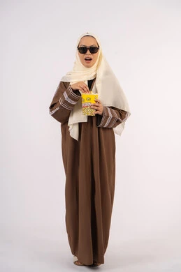 ايماءات المفاجأه والذهول، بورتريه لامرأة عربية خليجية اماراتيه محجبة ترتدي عباءه ، تحمل كيس الفوشار، متابعة الفيلم المفضل، التسلية والترفيه بقضاء أوقات ممتعة، الاستمتاع بمشاهدة الأفلام داخل السينما ، خلفية بيضاء