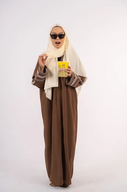 ايماءات الجودة والامتياز، متابعة الفيلم المفضل، التسلية والترفيه بقضاء أوقات ممتعة، بورتريه لامرأة عربية خليجية اماراتيه محجبة ترتدي عباءه ، تحمل كيس الفوشار وترفع يدها بتعابير الموافقة ، الاستمتاع بمشاهدة الأفلام داخل السينما ، خلفية بيضاء