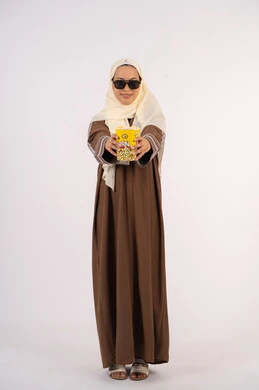 ارتداء نظاره سوداء ،التسلية والترفيه بقضاء أوقات ممتعة، الاستمتاع بتناول الفوشار ،متابعة الفيلم المفضل، الاستمتاع بمشاهدة الأفلام داخل السينما، بورتريه لامرأة عربية خليجية اماراتيه محجبة ترتدي عباءه ، تقدم كيس الفوشار ، خلفية بيضاء