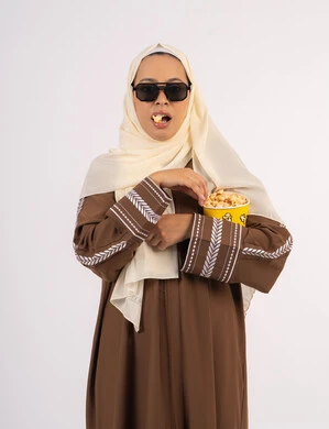 متابعة الفيلم المفضل، تعابير الاندماج والتفاعل ، الاستمتاع بمشاهدة الأفلام داخل السينما، بورتريه لامرأة عربية خليجية اماراتيه محجبة ترتدي عباءه ، وتأكل حبات الفوشار، التسلية والترفيه بقضاء أوقات ممتعة،  خلفية بيضاء