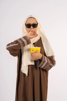 بورتريه لامرأة عربية خليجية اماراتيه محجبة ترتدي عباءه وتحمل كيس فوشار ، تعابير الارهاق والنعاس ، الاستمتاع بمشاهدة الأفلام داخل السينما، التسلية والترفيه بقضاء أوقات ممتعة، متابعة الفيلم المفضل، خلفية بيضاء