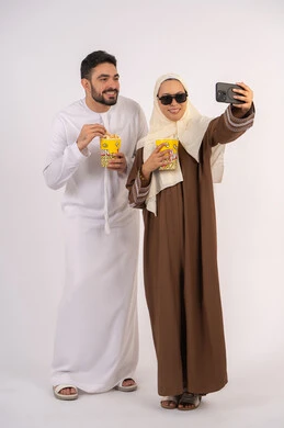 Enjoying popcorn, expressions of pleasure and happiness, portrait of a smiling Emirati Gulf Arab couple looking at the camera, enjoying family entertainment activities, watching movies and series, having a good time at the cinema, white background