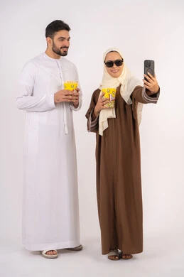 تعابير السرور والسعاده ، بورتريه لزوجيين عربيين خليجيين اماراتيين مبتسميين ينظران الى الكاميرا، الاستمتاع بالأنشطة العائلية الترفيهيه، تناول الفوشار اثناء متابعة الأفلام والمسلسلات، قضاء وقت ممتع في السينما،خلفية بيضاء