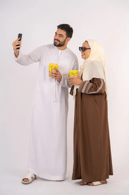 التقاط صور السيلفي ،بورتريه لزوجيين عربيين خليجيين اماراتيين مبتسميين ينظران الى الكاميرا، تعابير الاندماج والتفاعل،الاستمتاع بالأنشطة العائلية الترفيهيه، تناول الفوشار اثناء متابعة الأفلام والمسلسلات، قضاء وقت ممتع في السينما،خلفية بيضاء