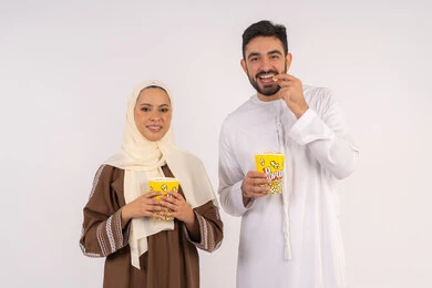 قضاء وقت ممتع في السينما، تناول الفوشار اثناء متابعة الأفلام والمسلسلات، بورتريه لزوجيين عربيين خليجيين اماراتيين مبتسميين ينظران الى الكاميرا بتعابير السرور والسعادة، الاستمتاع بالأنشطة العائلية الترفيهيه، خلفية بيضاء