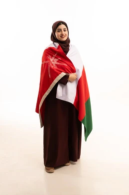 المشاركة بالاعياد والمناسبات الوطنية، الاحتفال بذكرى اليوم الوطني العماني، الاعتزاز والفخر بالرموز والراية العمانية، بورتريه لامراة لإمرأة عربية خليجية عمانية مبتسمة محجبة ترتدي العباءه تحمل علم سلطنة عمان، مفهوم حب الوطن والإنتماء إليه، الجسم بالطول الكامل، خلفية بيضاء