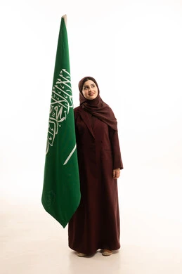 مفهوم حب الوطن و الانتماء اليه، يوم العلم السعودي11 مارس، ذكرى يوم بدينا 1727 م، الاحتفال بتأسيس الدولة السعودية الأولى 22 فبراير، بورتريه لإمرأة عربية خليجية سعودية ترتدي العباءة و الحجاب تمسك راية وشعار المملكة  تنظر الى شيء ما, الجسم بالطول الكامل, خلفية بيضاء