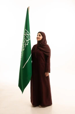 يوم العلم السعودي11 مارس, مفهوم حب الوطن و الانتماء اليه، ذكرى يوم بدينا 1727 م، الاحتفال بتأسيس الدولة السعودية الأولى 22 فبراير، بورتريه لإمرأة عربية خليجية سعودية ترتدي العباءة و الحجاب تمسك راية وشعار المملكة بايماءات الفخر, الجسم بالطول الكامل, خلفية بيضاء
