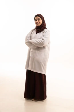 مهنة ووظيفة نسائية، العمل في القطاع الصحي في المملكة، مفهوم الطب والرعاية الصحية، بورتريه لطبيبة عربية خليجية سعودية ترتدي المعطف الطبي تقف بأيدي متقاطعة تنظر إلى الكاميرا بايماءات الثقة بالنفس، تقديم الخدمات للمرضى بكل كفاءة، الجسم بالطول الكامل، خلفية بيضاء