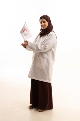 Working in the medical field, providing emergency medical services, looking at the camera with expressions of happiness, contributing to humanitarian and social services, the flag of the Saudi Red Crescent Authority, a portrait of a Saudi Arabian Gulf female doctor wearing a white coat and hijab holding the Red Crescent flag in her hands, full-body, white background.