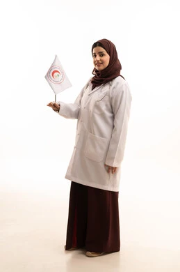 تقديم الخدمة الطبية الإسعافية الطارئة، النظر للكاميرا بتعابير السعادة، الإسهام في الخدمات الإنسانية والاجتماعية، علم هيئة الهلال الأحمر السعودي، العمل في المجال الطبي، بورتريه لطبيبة سعودية عربية خليجية ترتدي المعطف الأبيض والحجاب تمسك بيديها علم الهلال الاحمر، الجسم بالطول الكامل، خلفية بيضاء
