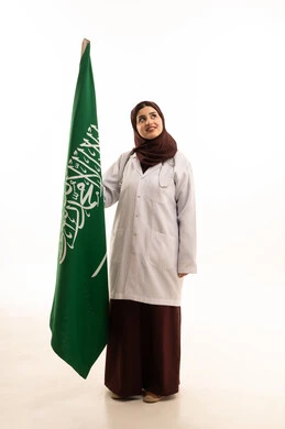 The anniversary of the unification of the Kingdom of Saudi Arabia, a portrait of a Saudi Arab female doctor wearing a gown and stethoscope holding the Saudi flag in her hands, celebrating the National Day with pride and dignity. The Saudi flag is the banner of unification and Islam, looking at something, full-body, white background.