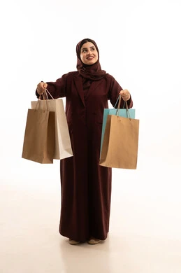Looking at something, the excitement to take advantage of discounts on products, a portrait of a smiling Saudi Arabian woman wearing an abaya holding paper bags in her hand, exploiting seasonal offers and discounts and Black Friday, shopping from commercial malls, expressions of happiness and joy, full-body, white background.