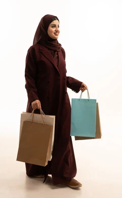ايماءات المشي والذهاب، الحماس للاستفادة من الخصومات على المنتجات ، بورتريه لامرأة عربية سعودية مبتسمة ترتدي العباءة تحمل بيدها أكياس ورقية, استغلال العروض والتخفيضات الموسمية والجمعة البيضاء، التسوق من المولات التجارية، تعابير السعاده و السرور، الجسم بالطول الكامل، خلفية بيضاء