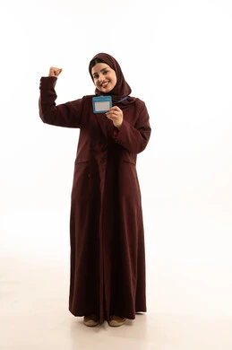 تعابير الفوز و اللنجاح ، عرض كرت فارغ مستطيل الشكل، موك اب ابيض، بورتريه لامرأة عربية سعودية مبتسمة ترتدي العباءة تحمل بيدها بطاقة تعريفية، النظر إلى الكاميرا بإيماءات السعادة والسرور، توضيح أهمية الهوية الشخصية، الجسم بالطول الكامل، خلفية بيضاء