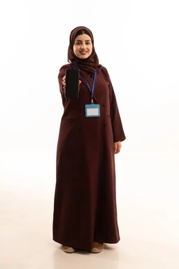 Spending enjoyable times exchanging news and conversations remotely, displaying a blank black screen, a portrait of a Saudi Arabian Gulf woman wearing a hijab and an abaya, holding a mobile phone with an identification card with a blue strip in her hands, full-body, white background.