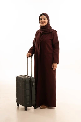 النظر  الكاميرا بتعابير السعادة ، التجهيز للسفرات الممتعة, الاستمتاع بالرحلات السياحية في وقت العطلة, بورتريه لامرأة عربية خليجية سعوديه محجبة ترتدي العباءة تمسك بيدها حقيبة سفر, الجسم بالطول الكامل, خلفية بيضاء