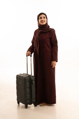 النظر الى شيء ما ، التجهيز للسفرات الممتعة, الاستمتاع بالرحلات السياحية في وقت العطلة, بورتريه لامرأة عربية خليجية سعوديه محجبة ترتدي العباءة تمسك بيدها حقيبة سفر , إيماءات السعادة والسرور, الجسم بالطول الكامل, خلفية بيضاء