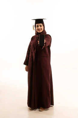 Online study applications, a display of a blank black screen on a mobile phone, a portrait of a young Arab Gulf Saudi woman wearing a hat and an abaya holding a mobile phone in her hand, expressions of happiness and joy, celebrating the completion of the university stage, full-body shot, white background.
