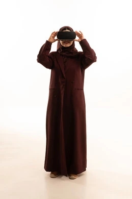 استخدام الأجهزة التقنية الحديثة والتكنولوجيا في رؤية المشاهد الخيالية، قضاء أوقات الفراغ بشكل ممتع، إيماءات التفاعل والاندماج مع الواقع الافتراضي، بورتريه لامرأة عربية خليجية سعودية ترتدي العباءة و الحجاب تضع نظارات الفي آر، الجسم بالطول الكامل، خلفية بيضاء