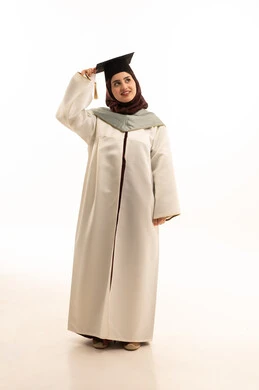Celebrating the completion of university studies, the concept of diligence and excellence, expressions of joy and happiness at achieving the dream of success, and a portrait of a Saudi Arabian Gulf female graduate wearing a white graduation gown, holding a graduation cap in her hand, looking at the camera with gestures of joy and pride, full-body shot, white background.