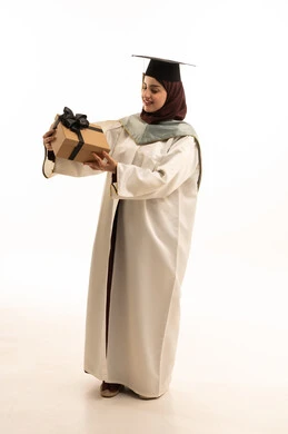 The concept of diligence and excellence, celebrating the completion of university studies, a portrait of a Saudi Arabian Gulf female graduate wearing a white abaya and graduation cap, holding a gift in her hand, looking at it with gestures of satisfaction and joy, education in the Kingdom of Saudi Arabia, full-body shot, white background.
