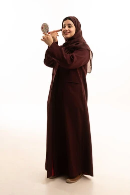 الاهتمام بالجمال والمظهر الخارجي, التسويق لمنتجات ومستحضرات التجميل المحلية, الشغف بوضع الميك اب، مفهوم التزين والتجمل, بورتريه لامرأة عربية خليجية سعودية ترتدي الحجاب و العباءة تقوم باستخدام فرشاة أحمر الخدود، الجسم بالطول الكامل، خلفية بيضاء