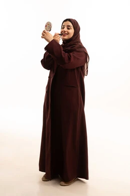 Women's cosmetic products, a portrait of a Saudi Gulf Arab woman wearing a hijab and abaya holding beauty tools in her hand, marketing for cosmetic products, the concept of caring for beauty and skin, using lipstick, full-body, white background.