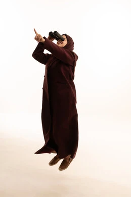 Seeing distant things, thinking and looking forward to the future, future planning for goals and ambitions, a portrait of a young Arab Gulf Saudi woman wearing a hijab and an abaya, jumping in the air holding binoculars, looking at something and pointing at it, full-body, white background.