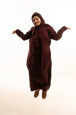 موضوع مبهم و مجهول، بورتريه لشابة عربية خليجية سعودية محجبة ترتدي عباءة تقفز في الهواء ترفع كفات يدها لأعلى بإيماءات و تعابير وجه ويدين تدل على عدم المعرفة أمر ما ، لا تعلم شيئاً  ، الجسم بالطول الكامل، خلفية بيضاء